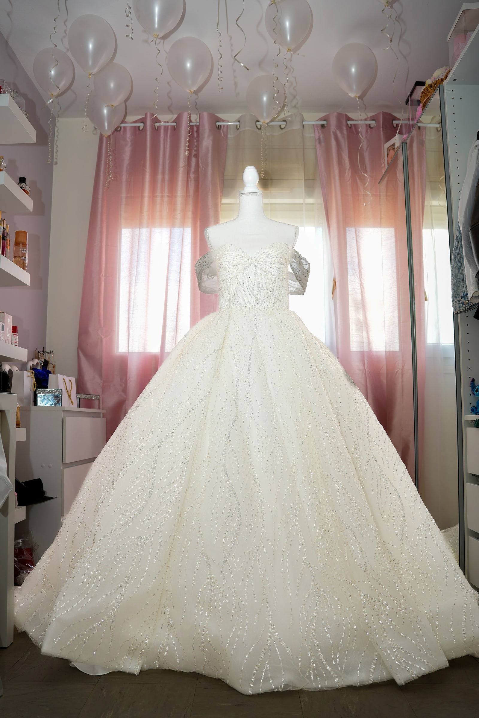 La robe de mariée sur son buste, devant des rideaux roses