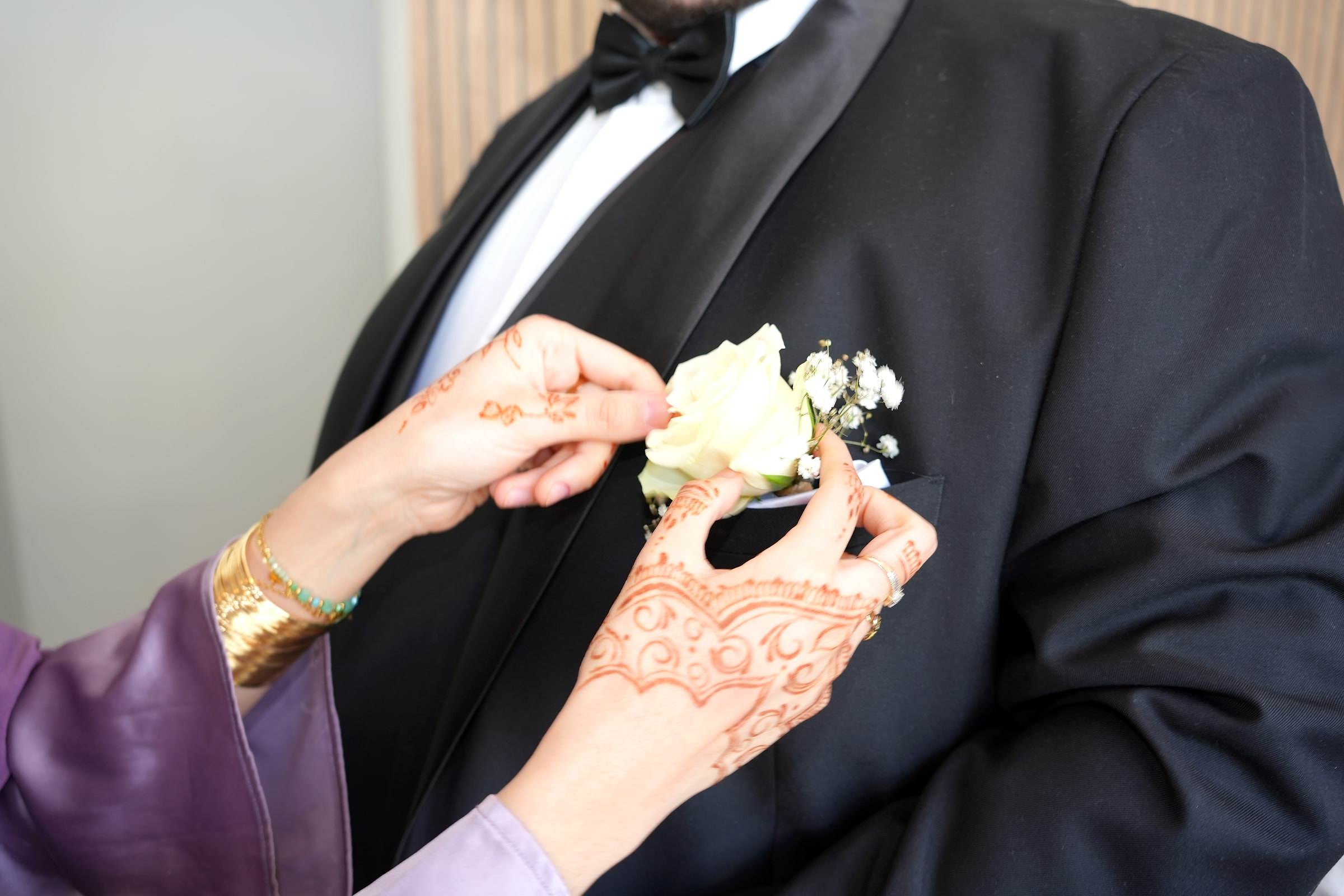 Une main ornée de henné épingle la boutonnière du marié