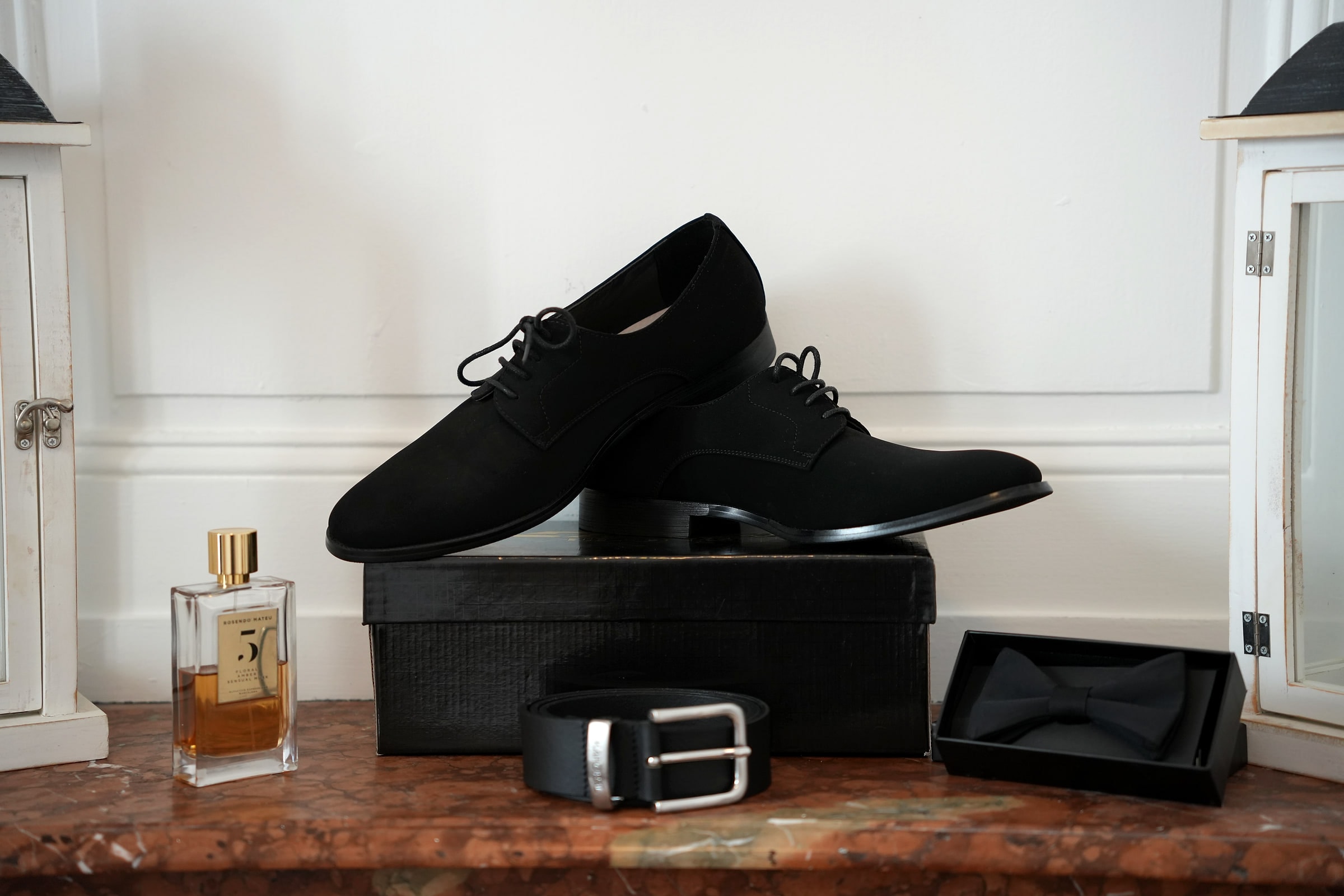 Les chaussures, la ceinture, le nœud papillon et le parfum du marié sur une cheminée de marbre