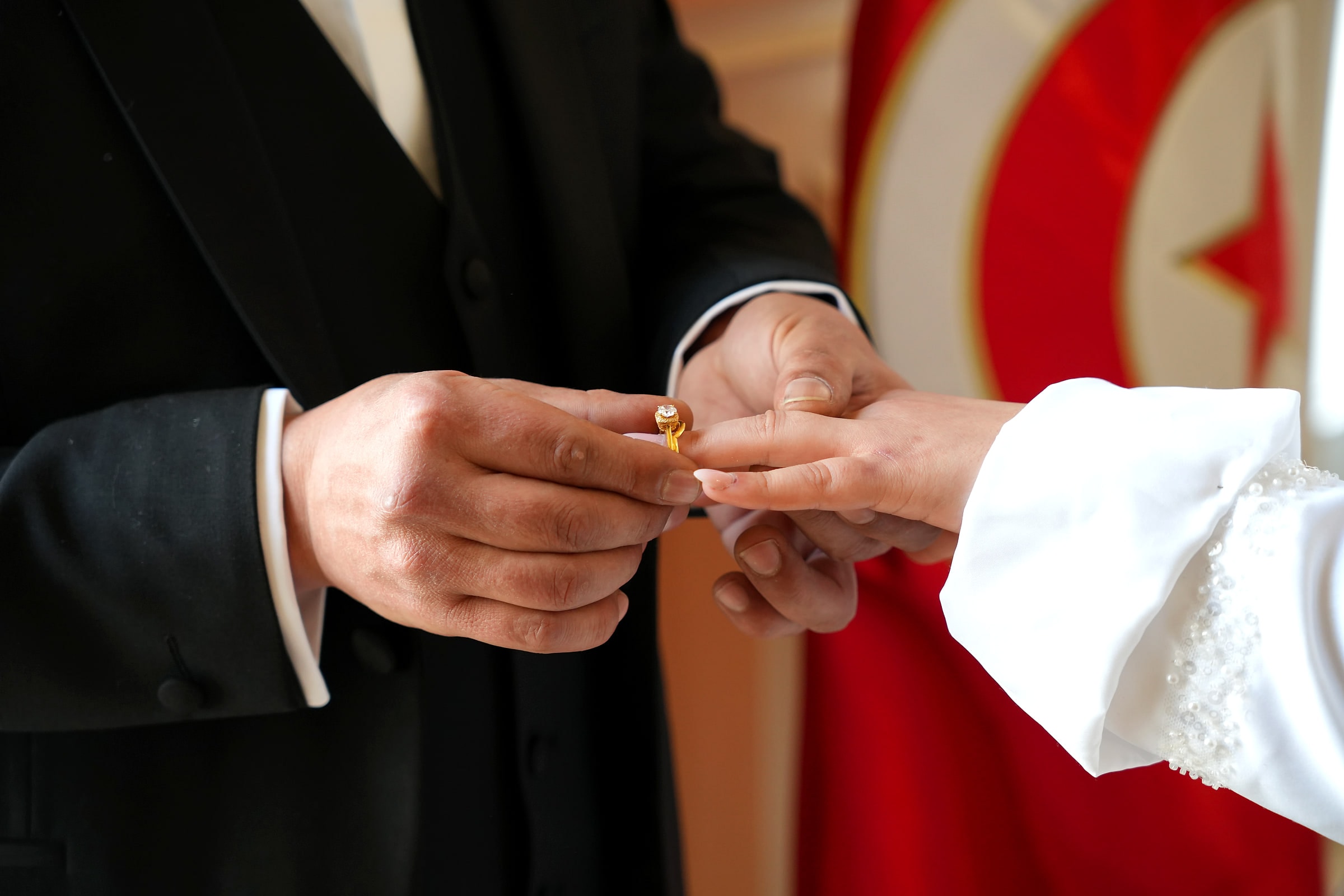 Le marié glisse l’alliance au doigt de la mariée, devant le drapeau tunisien